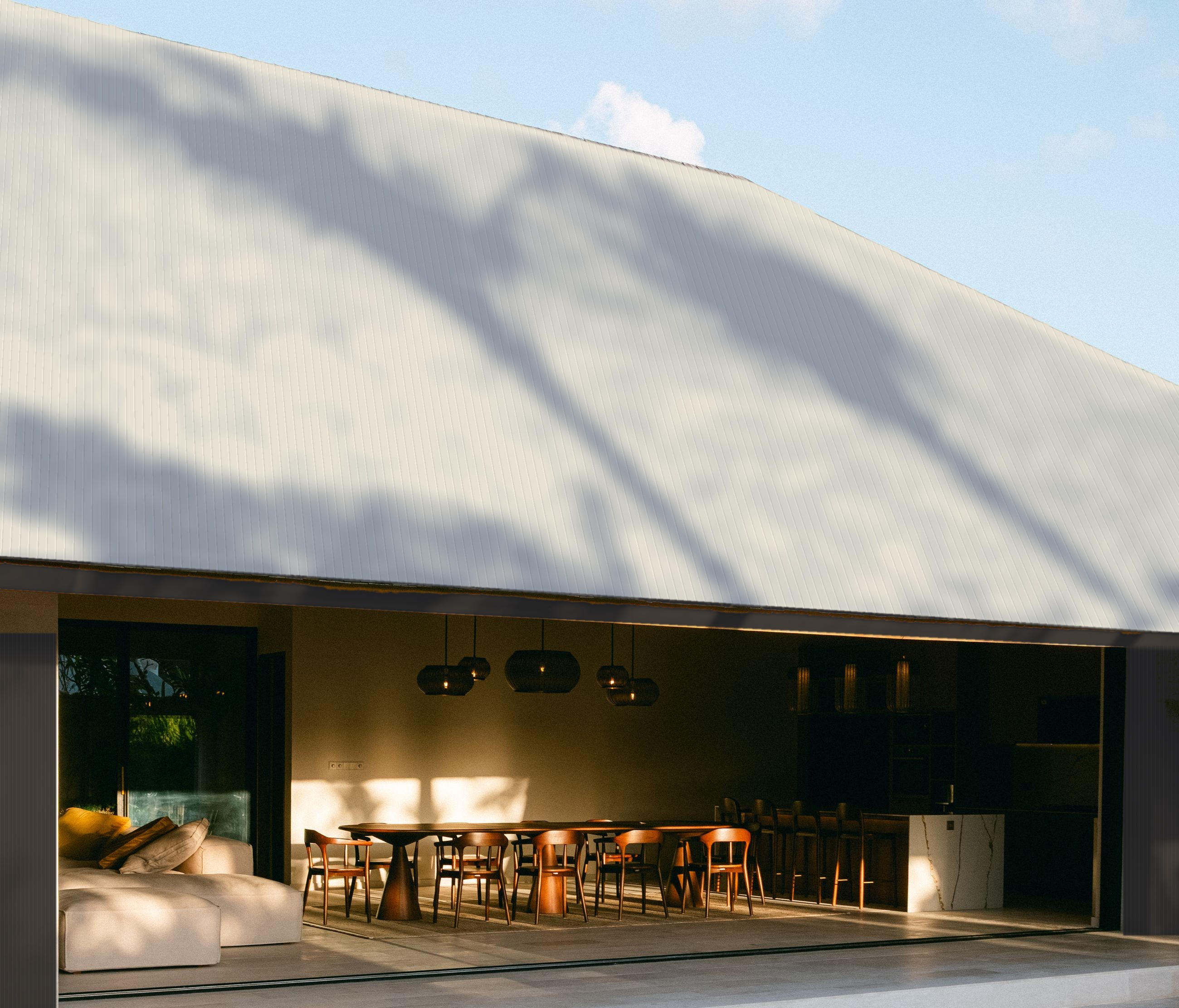 An open-air pavilion under a pale Surfmist roof with black walls, palm shadows falling across it in late light